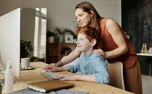 Une professeur aidant un enfant devant un pc